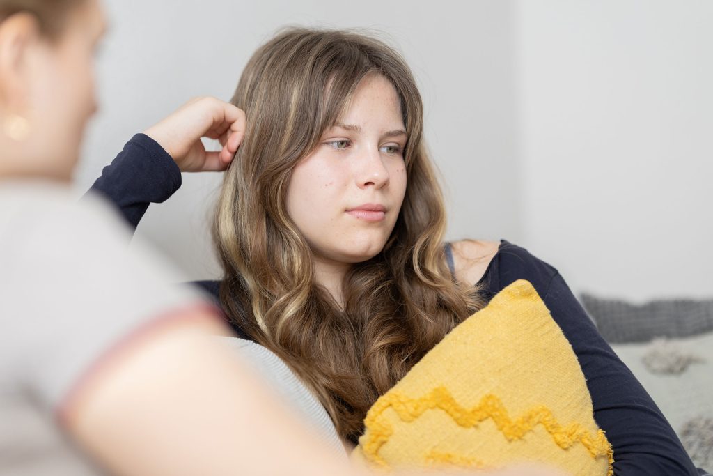 Young person sitting on a couch holding a yellow cushion, looking thoughtful during a counselling session