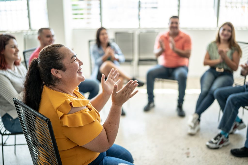 Group of adults sitting in a circle, smiling and clapping during a group session