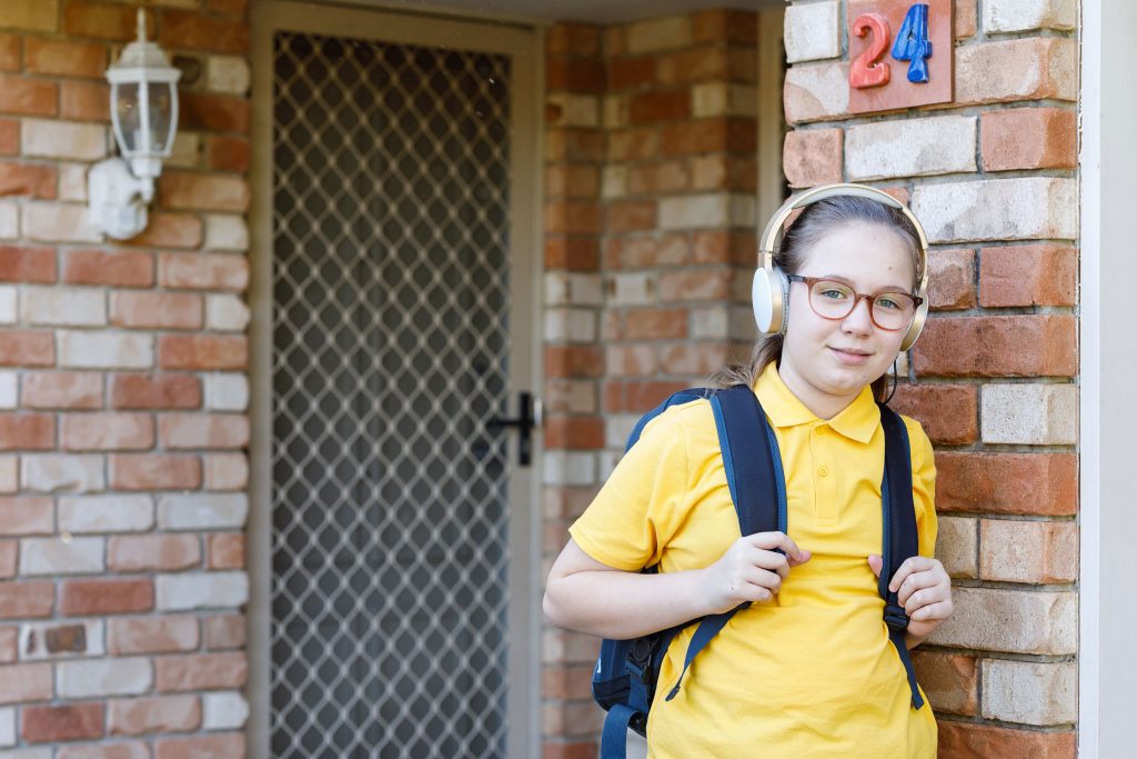 Young person wearing headphones and a backpack standing at a front door, ready to head out